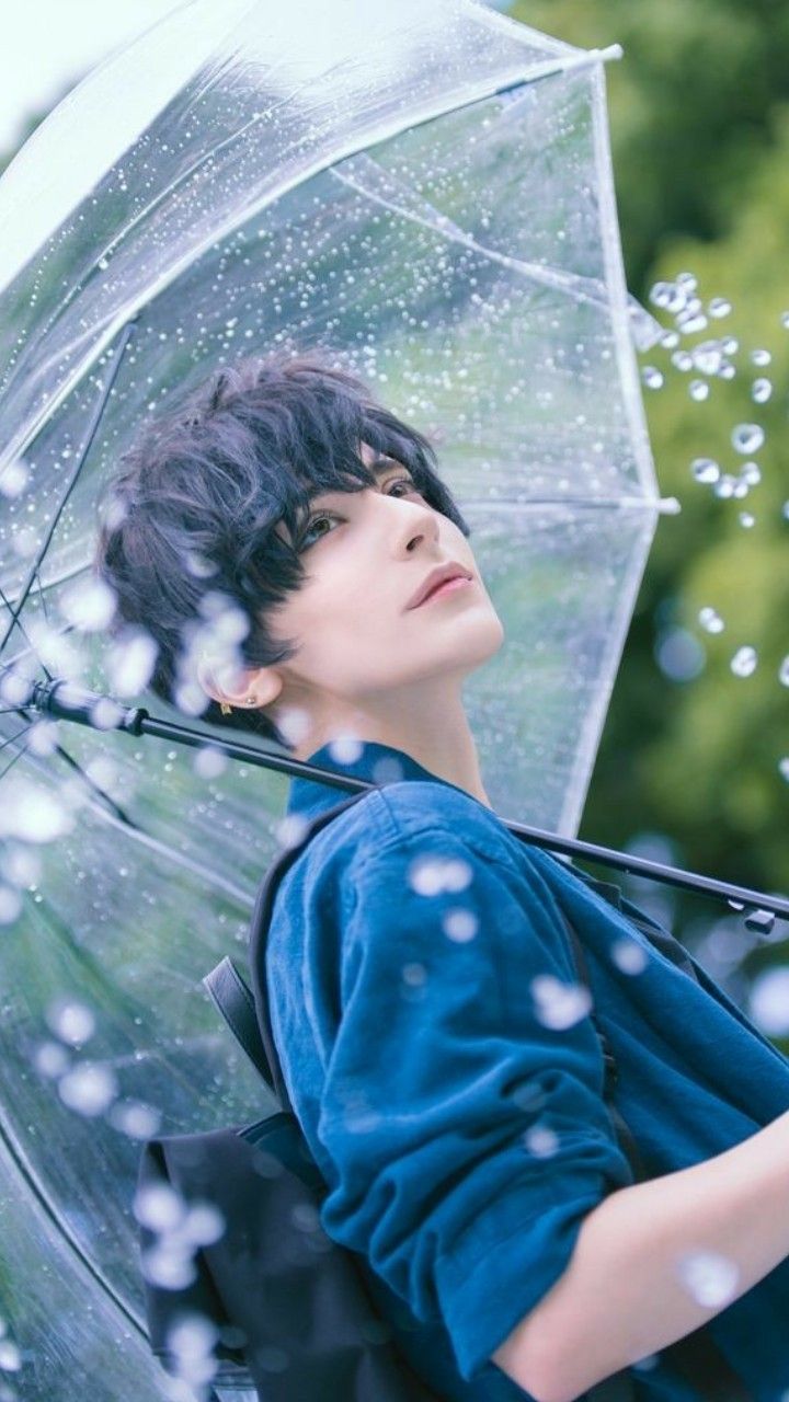 a young man holding an umbrella while standing in the rain with water droplets on it