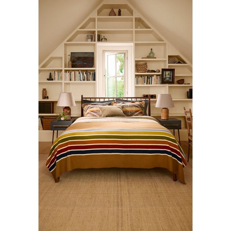 a bed sitting under a window in a bedroom next to a book shelf filled with books