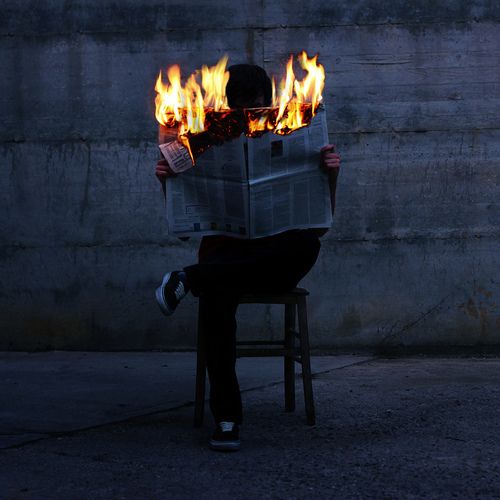 a person sitting on a stool reading a newspaper with fire coming out of their face