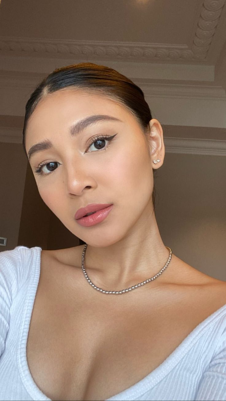 a woman wearing a white shirt and silver necklace looking at the camera with an intense look on her face