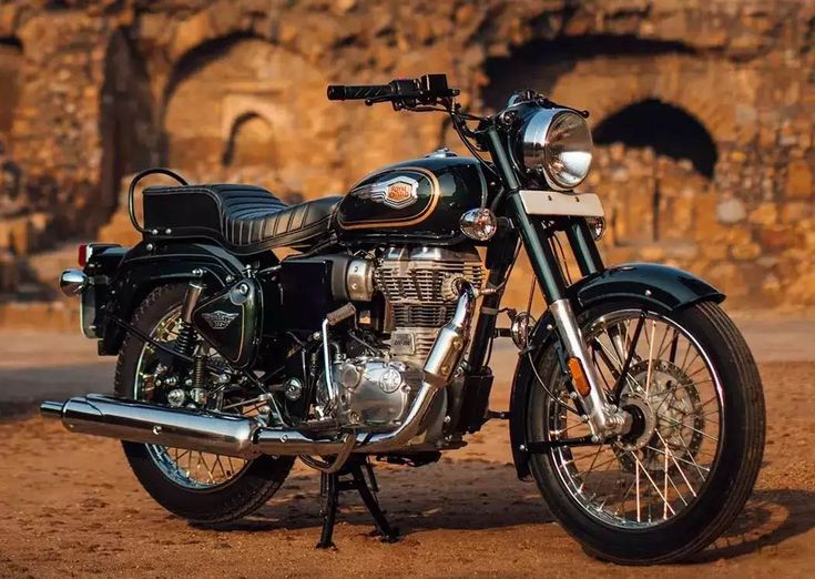 a black motorcycle parked on top of a dirt field next to a stone wall and tunnel