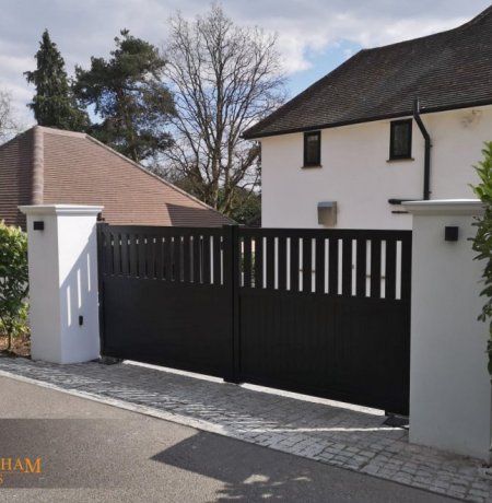 a white house with black gate and brick driveway