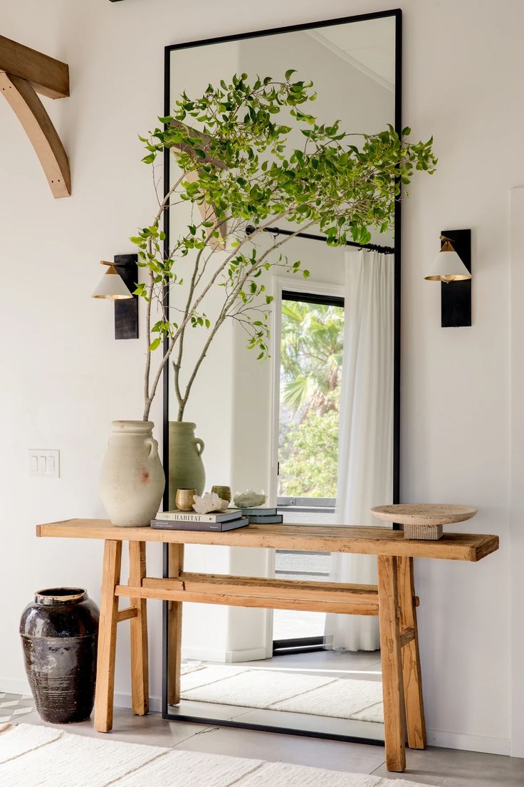 a table with a mirror and vases on it in front of a wall mounted plant