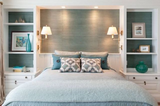 a bed with blue and white pillows in a bedroom next to two lamps on either side of the headboard