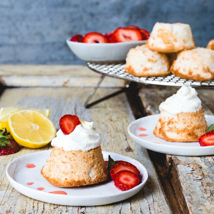 two small desserts on plates with strawberries and lemon wedges in the background