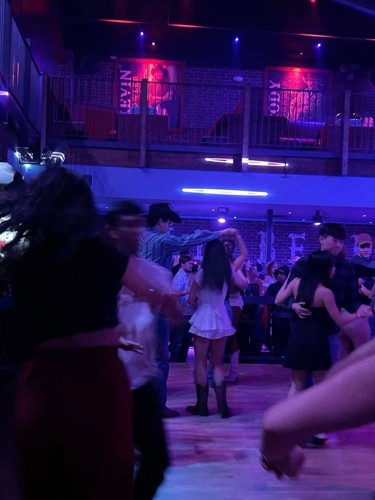 a group of people dancing in a large room with purple lights on the ceiling and floor