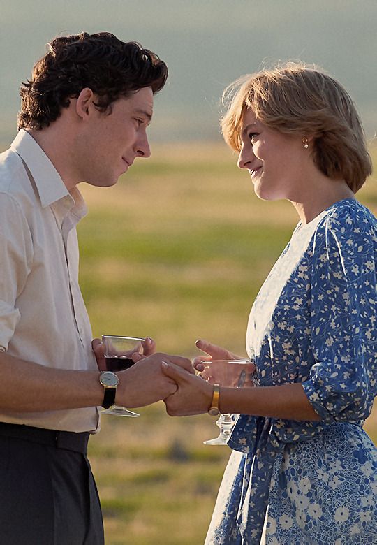 a man and woman standing next to each other holding wine glasses in their hands while looking at each other