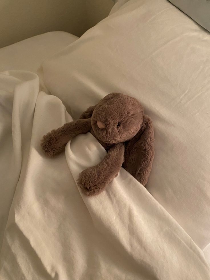 a brown teddy bear laying on top of a white bed