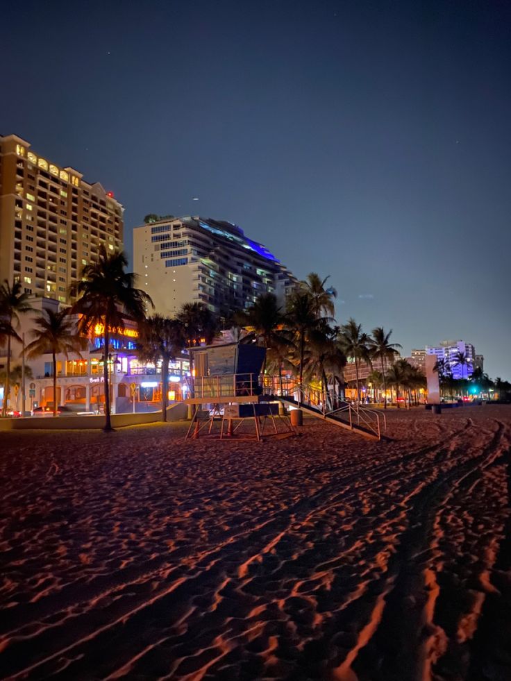 an empty beach at night with palm trees and buildings in the backgrouds