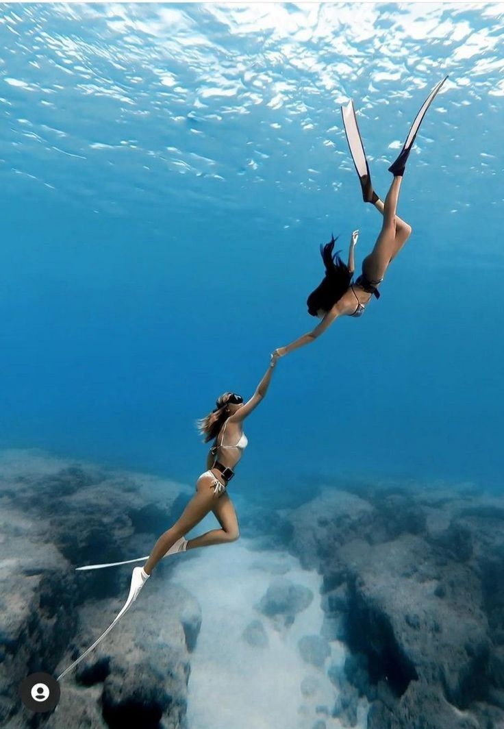 two women in bikinis hold up their skis under the water