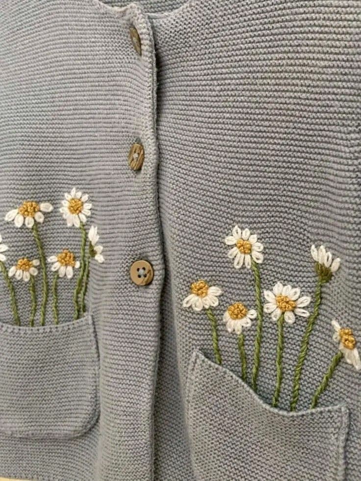 a sweater with daisies embroidered on the front and back pocket, along with buttons