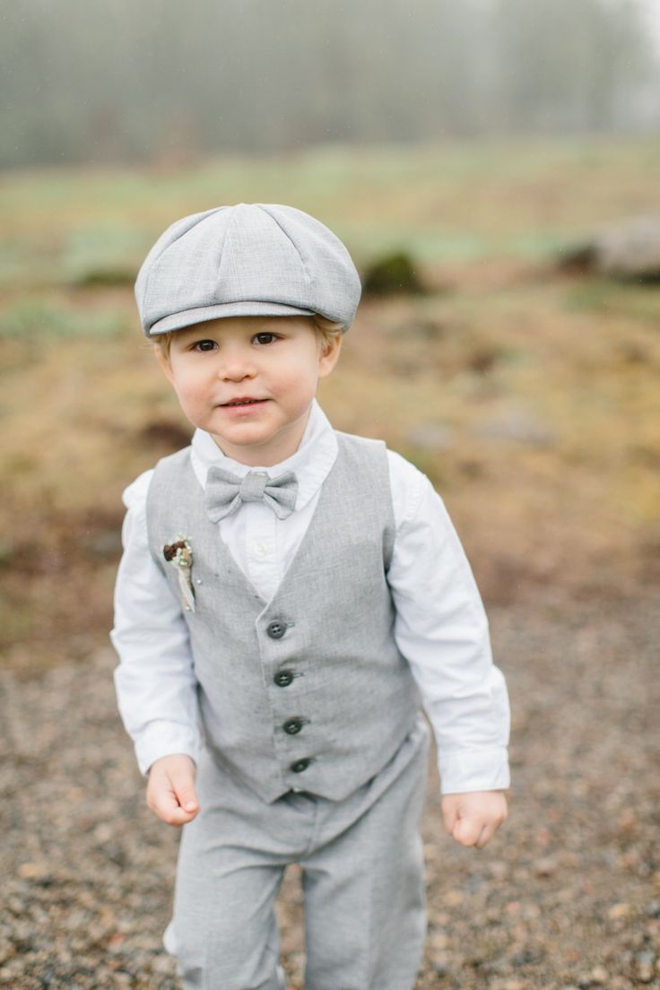 a young boy wearing a gray suit and bow tie standing in the middle of a field