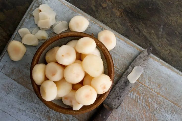 a bowl filled with peeled potatoes on top of a cutting board next to a knife