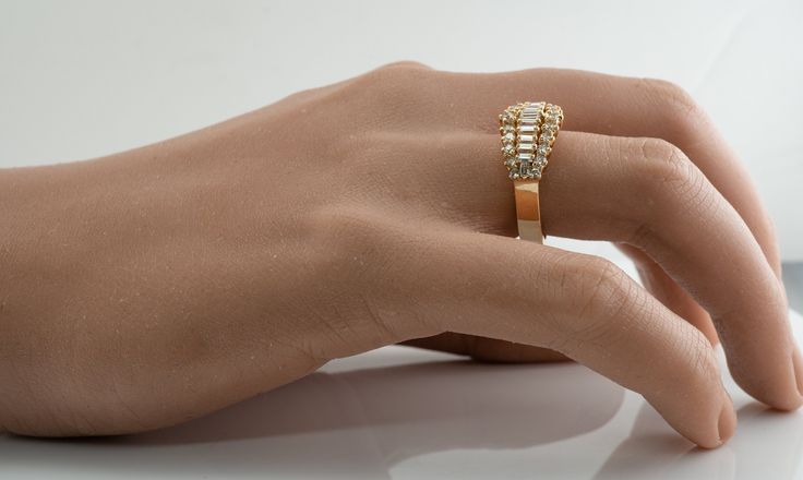 a woman's hand with a gold ring on top of her finger and an empty white surface behind it