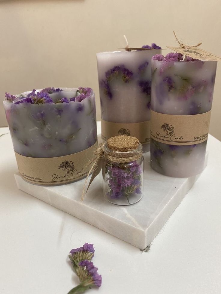 three candles sitting on top of a white table next to lavender flowers and a jar