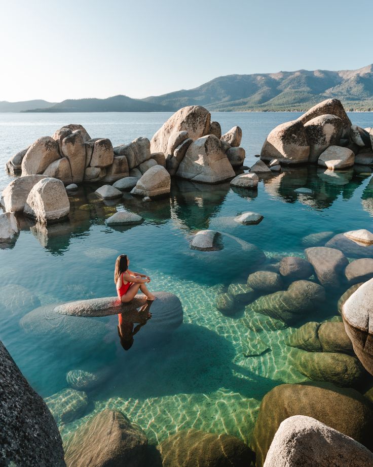 a woman is sitting on rocks in the water