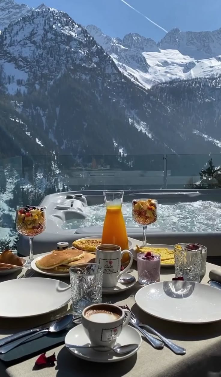 a table with plates and cups on top of it in front of snow covered mountains