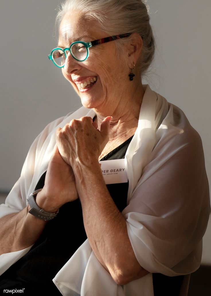 an older woman with glasses smiling and holding her hands together