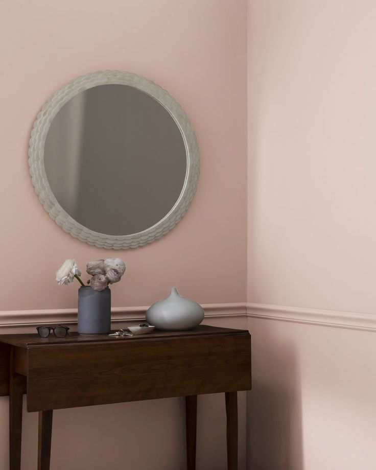 a table with a vase and mirror on it in front of a wall painted pink