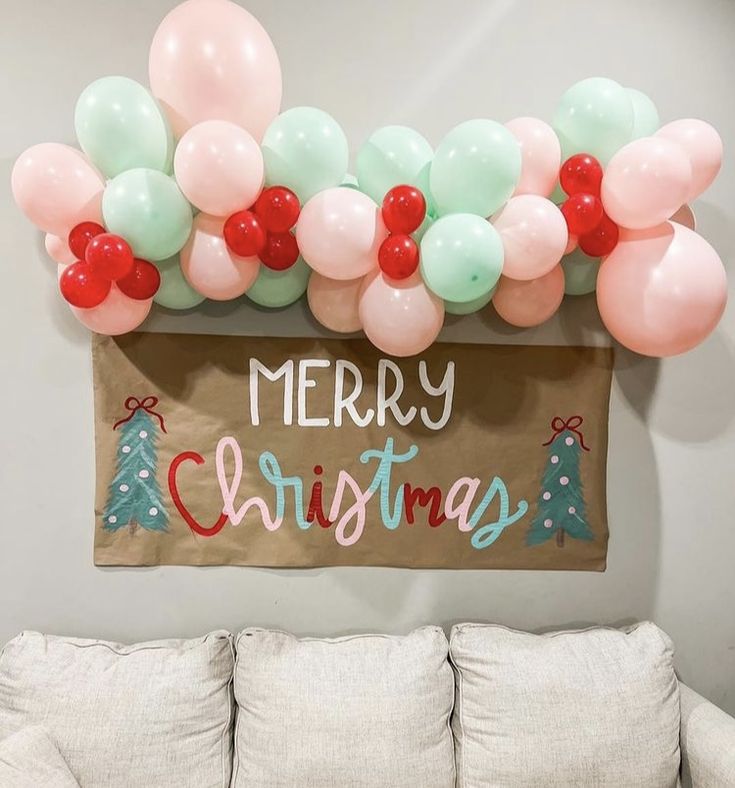 a merry christmas sign with balloons hanging on the wall and a couch in front of it