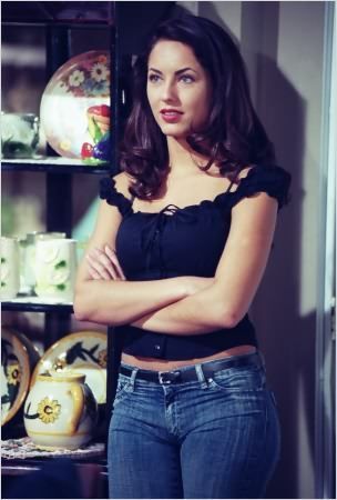 a woman standing in front of a book shelf with her arms crossed and looking at the camera