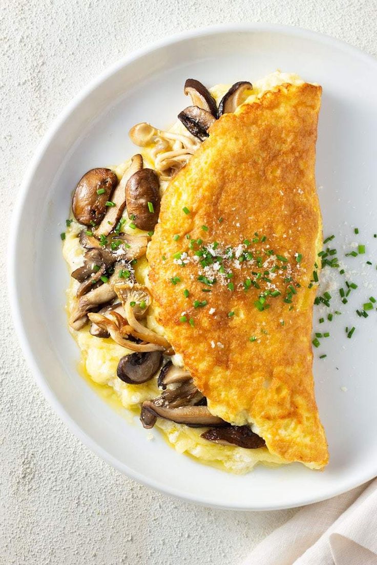 a white plate topped with an omelet covered in mushrooms