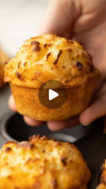 a person holding a muffin in their hand with other muffins around it