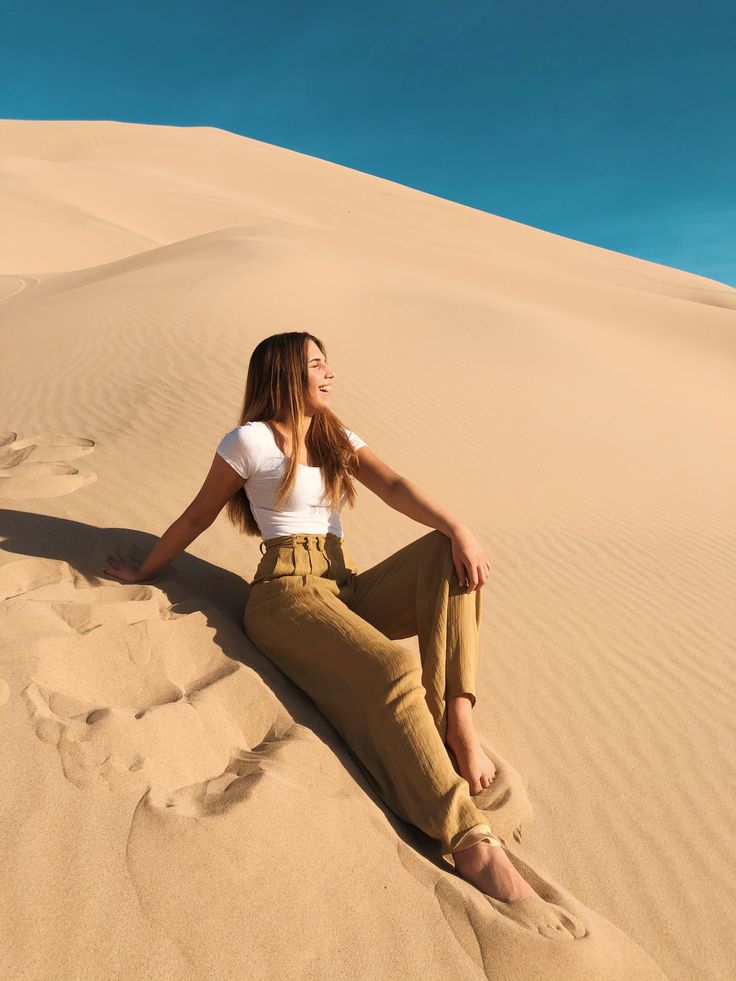 a woman sitting on top of a sandy dune