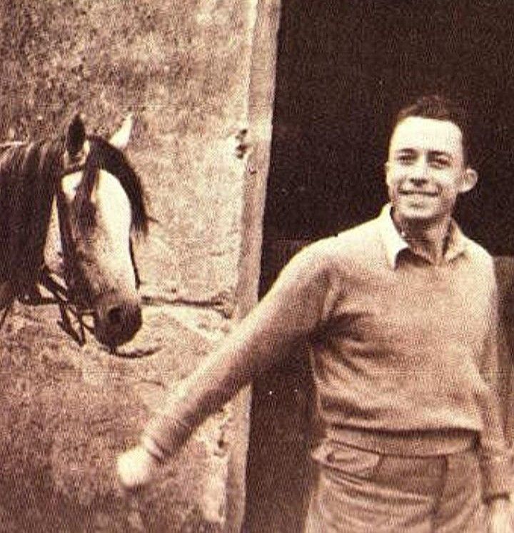 an old photo of a man standing next to a horse