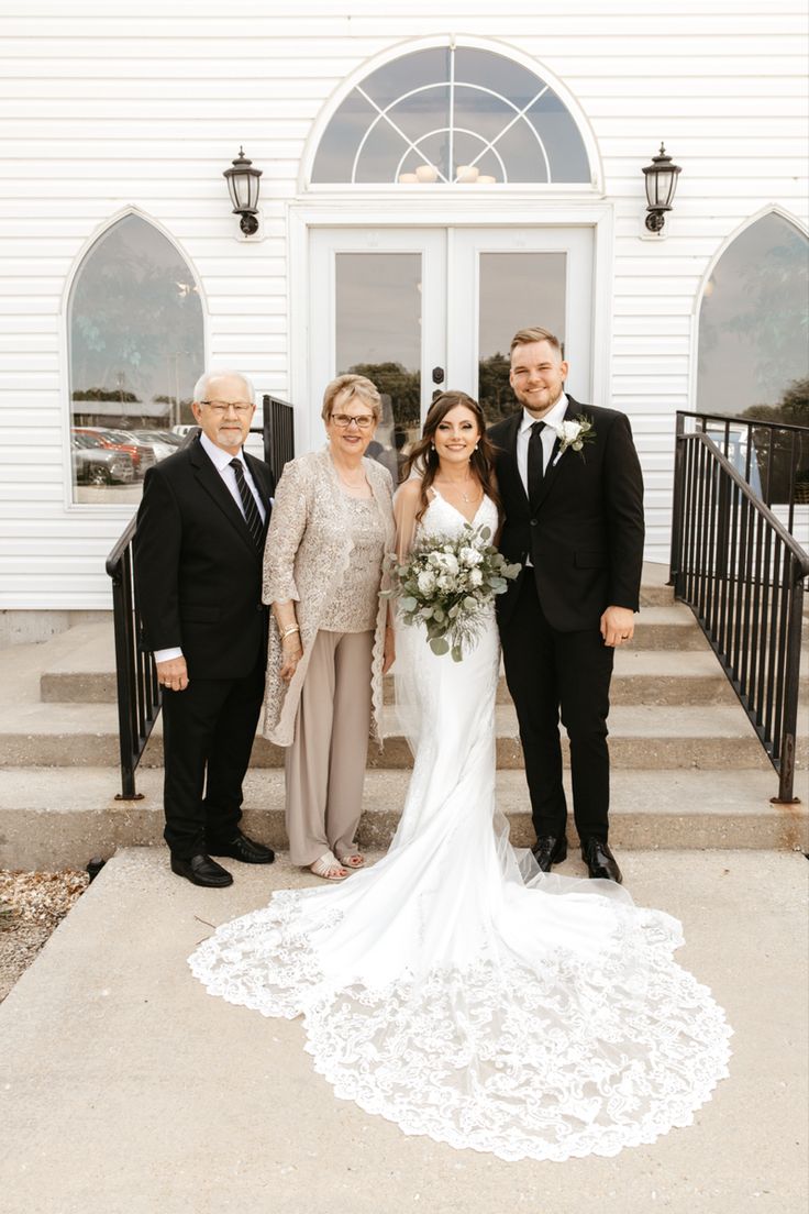 the bride and groom are posing for a photo with their parents on the front steps