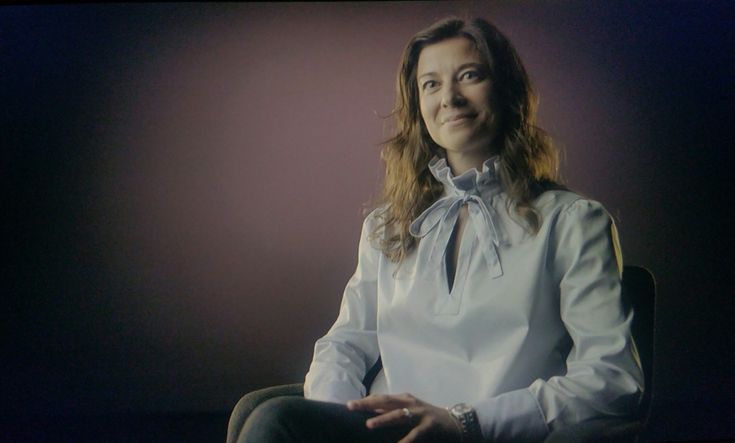 a woman sitting in a chair wearing a white shirt with a bow on her neck