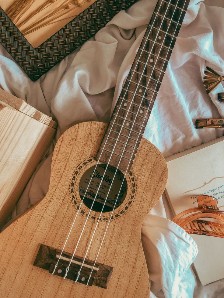 a wooden ukulele sitting on top of a bed next to an open book