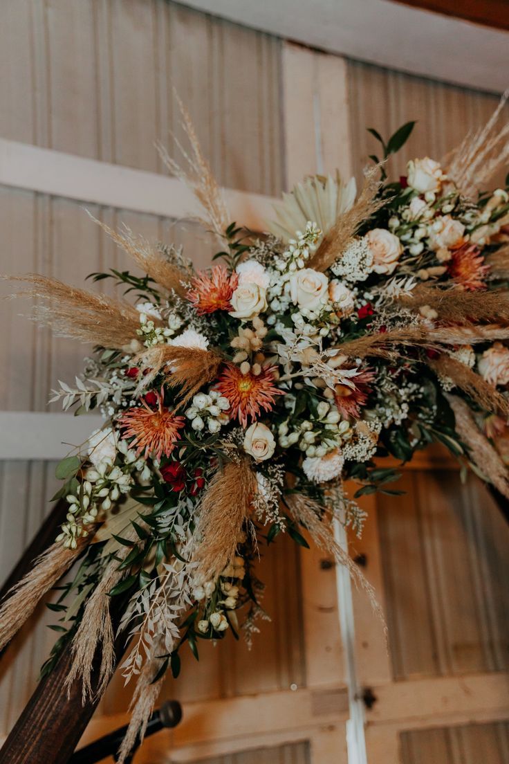 an arrangement of dried flowers and grasses is displayed on a pole in front of a wooden door