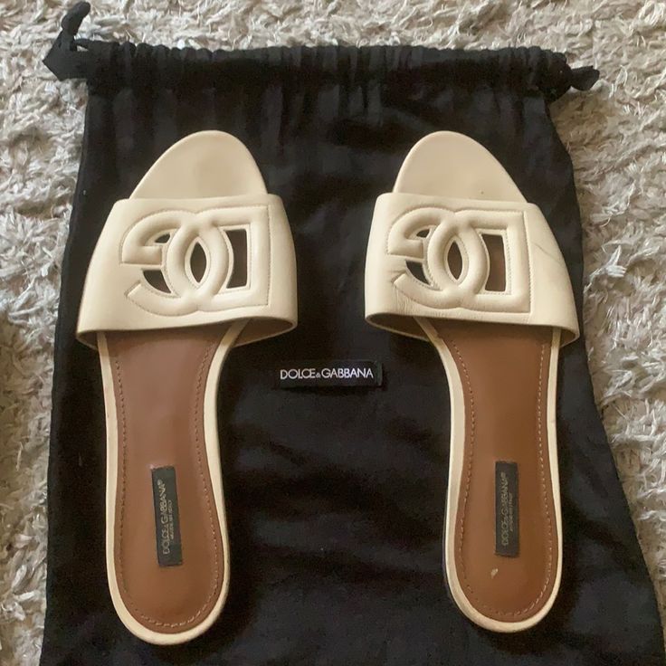 In Beige Luxury Cream Mules, Beige Flat Sandals For Evening, Designer Slip-on Sandals With Branded Insole, Designer Flat Slides For Beach, Luxury Flat Mules For Spring, Designer Leather Sandals For Vacation, Elegant Beige Leather Slides, Designer White Mules For Summer, Designer Open Toe Slides For Vacation