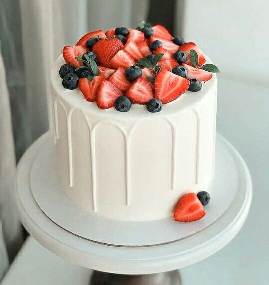 a white cake with strawberries and blueberries on top is sitting on a stand