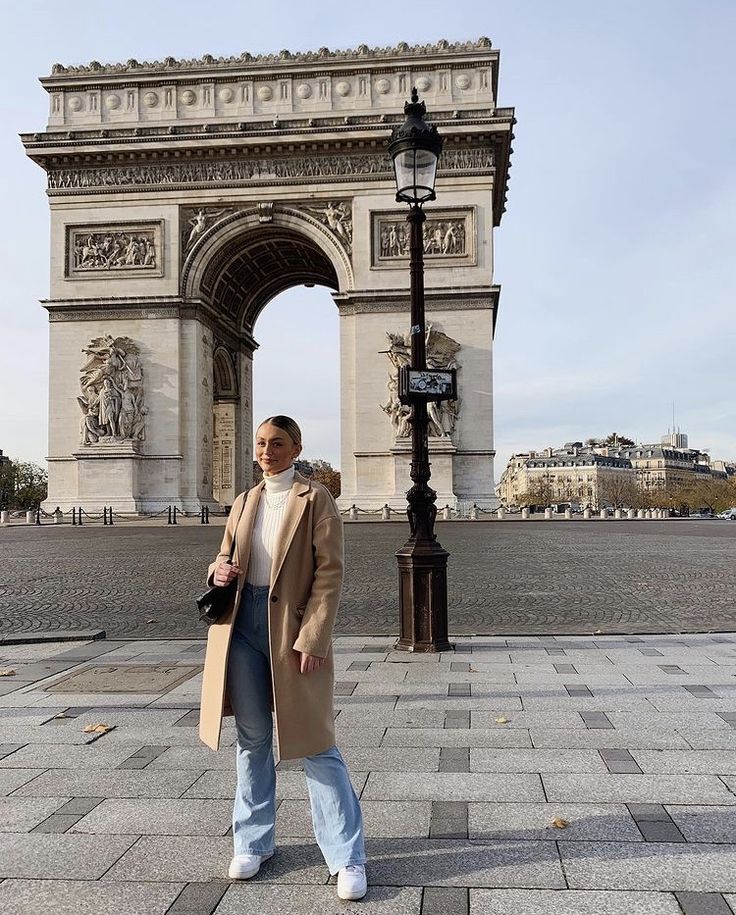 a man is standing in front of the arc de trio triumphe, with his coat over his shoulders