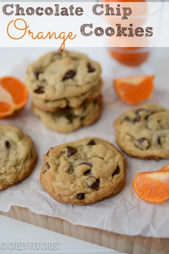 chocolate chip orange cookies are arranged on a piece of parchment paper with an orange slice next to them