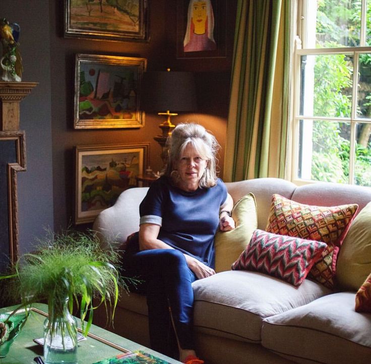 an older woman sitting on a couch in front of a window next to a potted plant