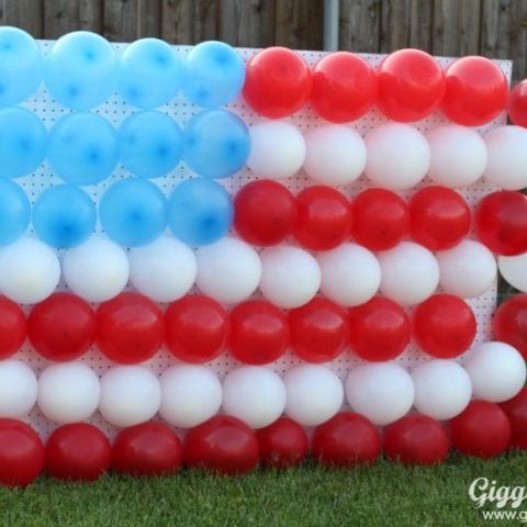 an american flag made out of balloons on the grass with a fence in the background