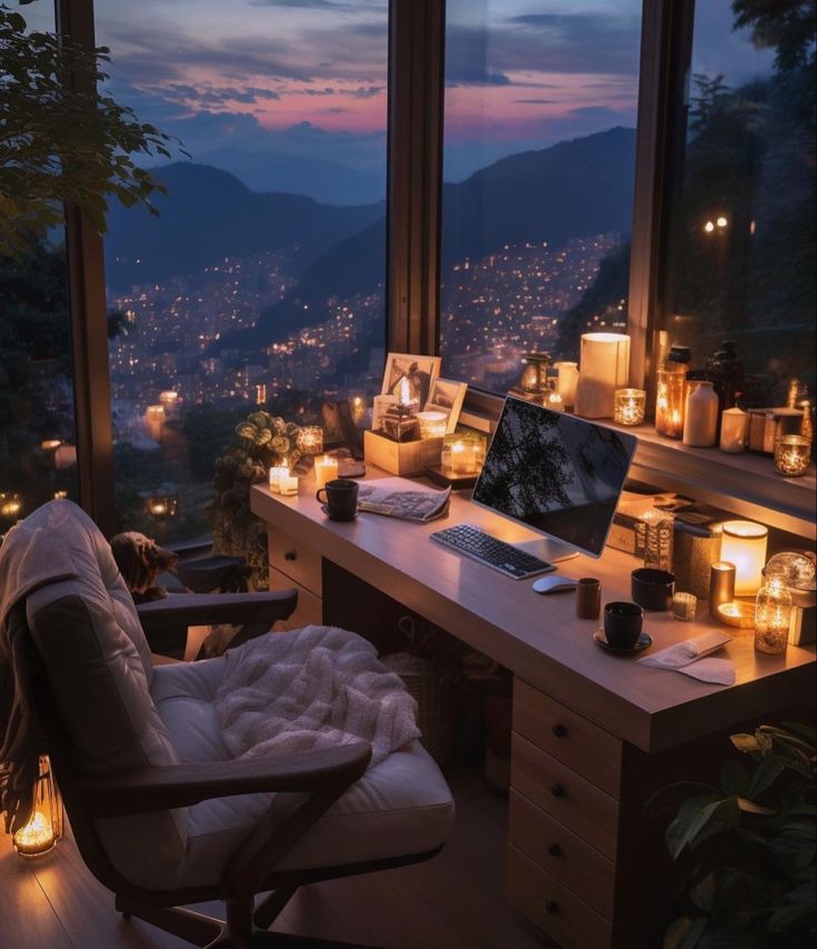 a desk with a laptop on it in front of a window filled with lit candles