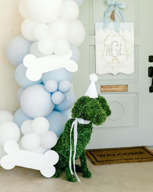 a dog made out of grass and balloons in front of a door with a party hat on it