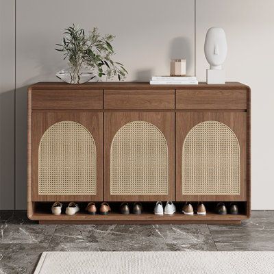 a wooden cabinet with several pairs of shoes on the bottom shelf and a potted plant next to it