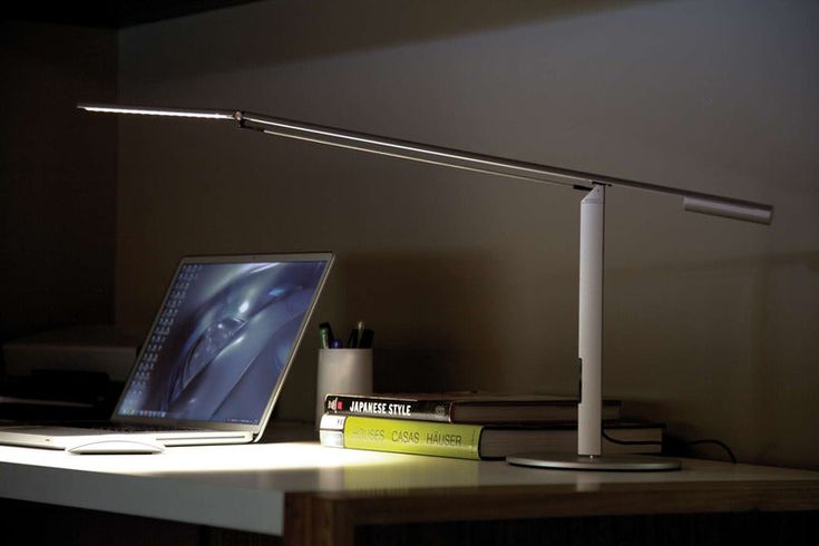 a laptop computer sitting on top of a desk next to a lamp and bookshelf