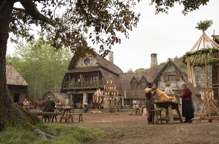 two people standing in front of an old fashioned village with lots of wood and stone buildings