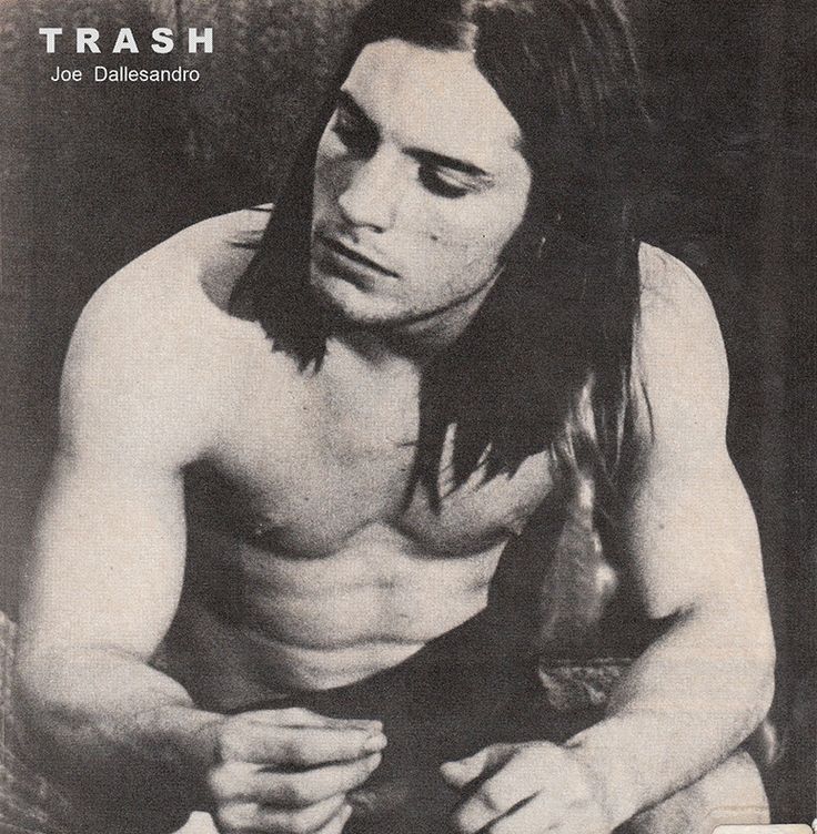 a shirtless man with long hair and no shirt sitting on the ground looking down