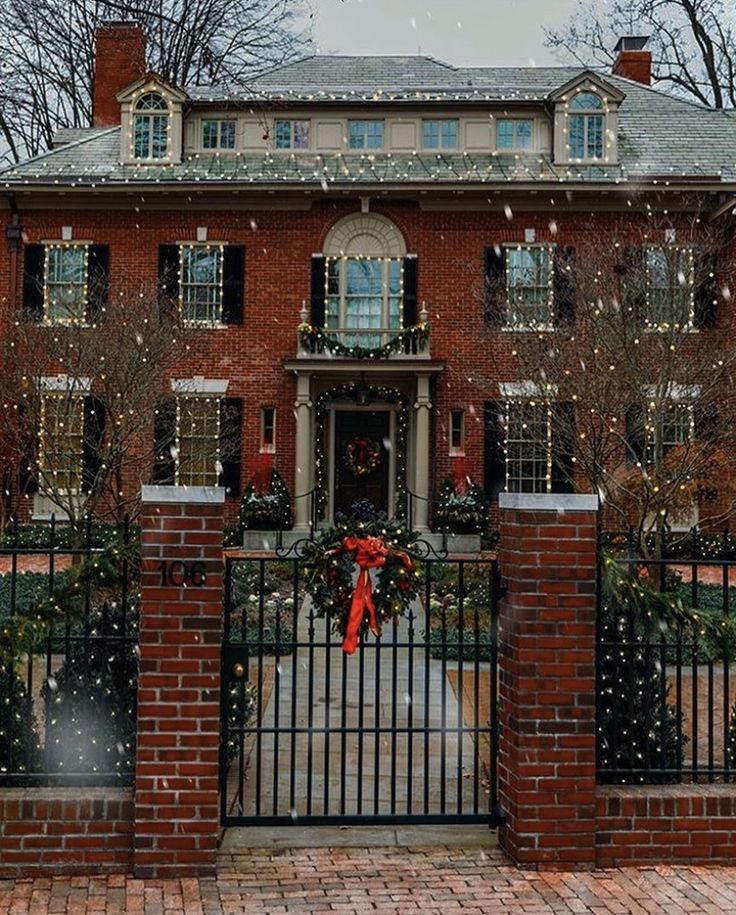 a red brick house with christmas wreaths on the front gate and trees behind it