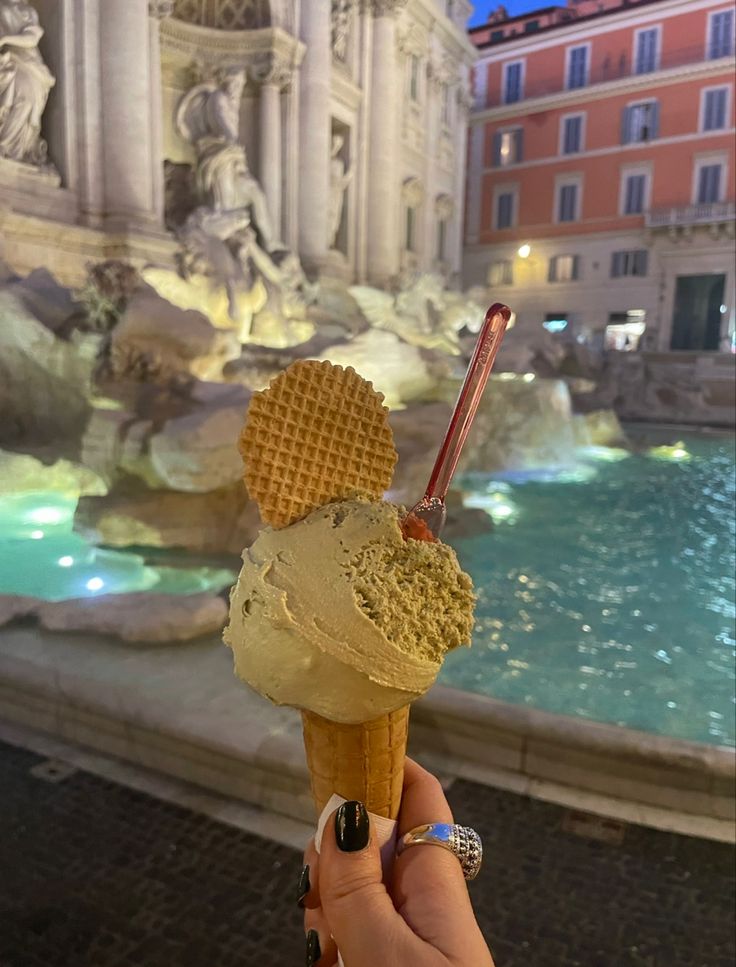 a person holding an ice cream cone in front of a fountain