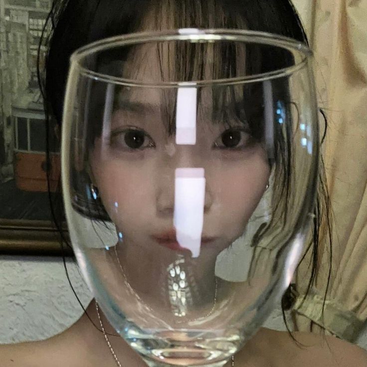 a young woman is holding a wine glass with the reflection of her face in it