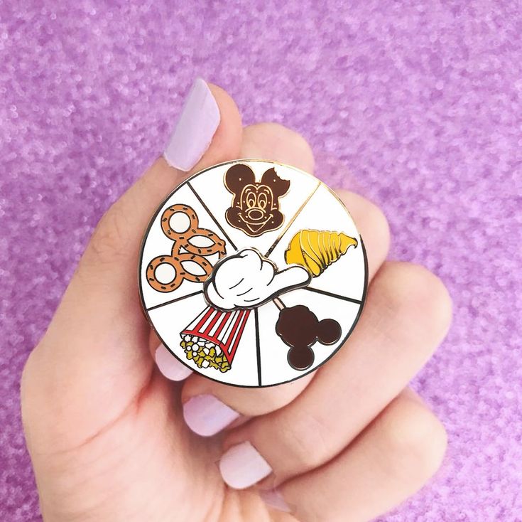 someone is holding a pin with mickey mouse and other things on it in their hand