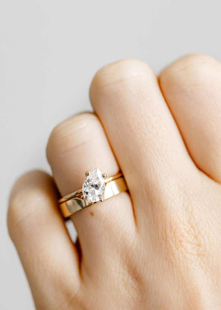 a woman's hand wearing a gold ring with a single diamond on it,